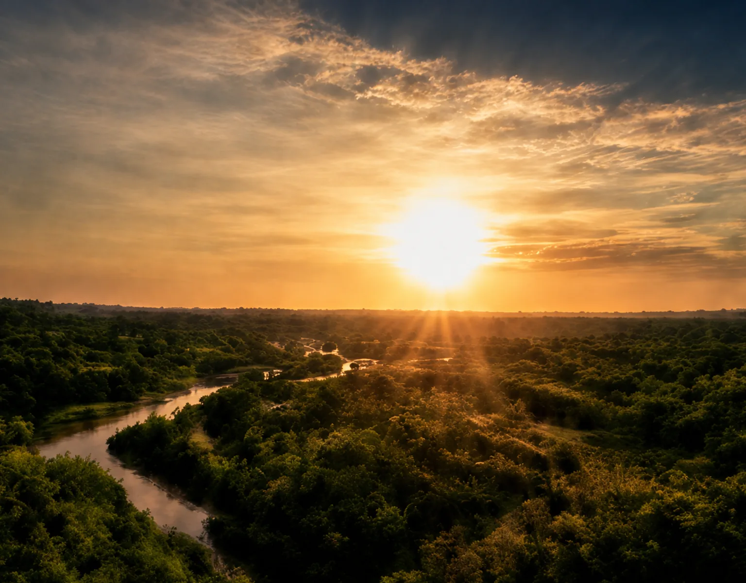 Vista aérea de um rio sinuoso entre vegetação verde em Barreiras, com pôr do sol dourado e céu dramático.